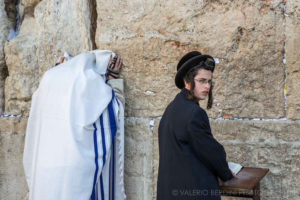 上图：哭墙晨祷。左边的男人披着祷告巾（Tallit Shawl），右手缠着经文匣（Arm Tefillin）。右边的男孩前额头上戴着经文匣(Head Tefillin）。经文匣里面藏着「示马」经文（申六4-9；十一13-21）。