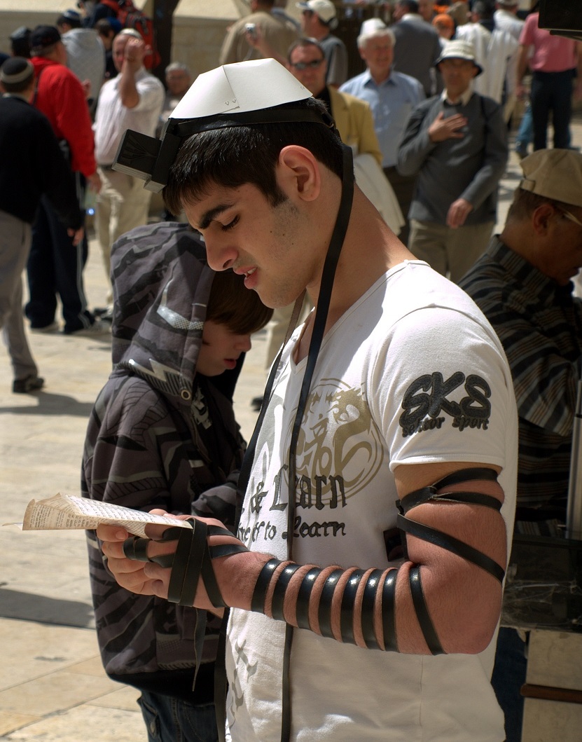 上图：一个犹太年轻人在前额和左臂上佩带经文匣（Tefillin），在耶路撒冷哭墙祷告。